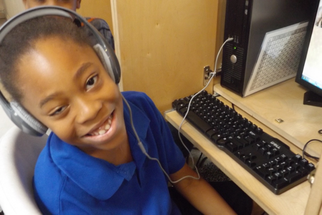 A boy in headphones beaming at his desk during a lesson.