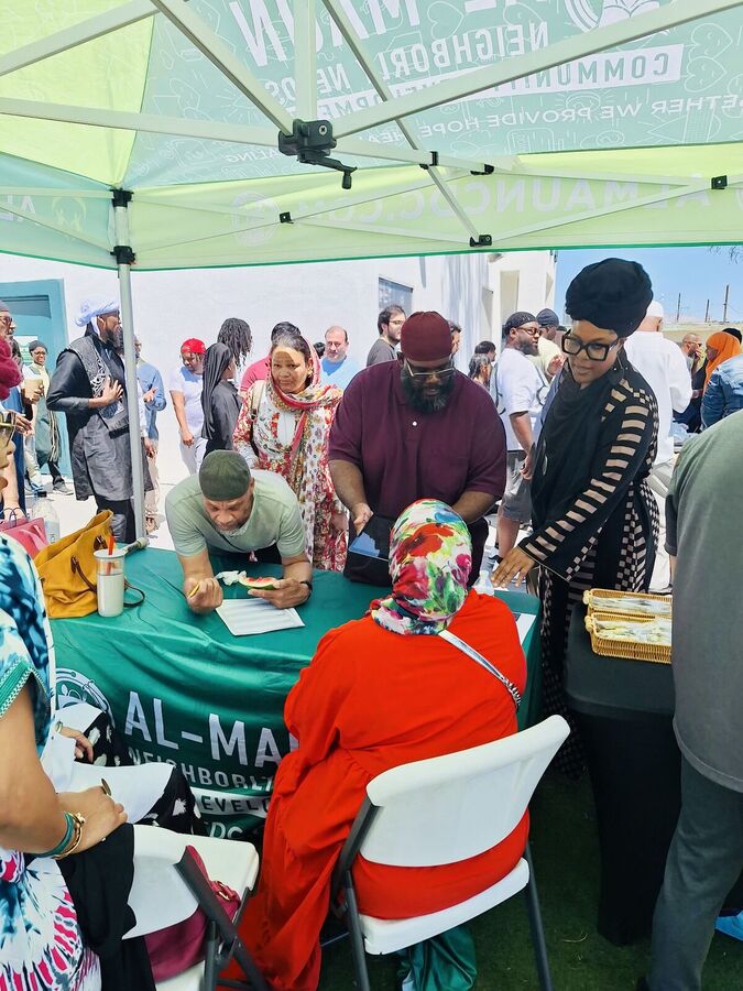 Neighbors gathered around a table under a green Al-Maun tent.